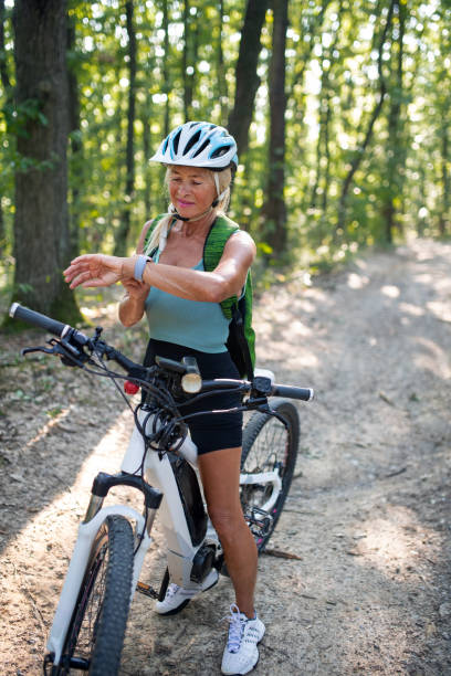istock Active senior woman biker sitting on bicycle and setting smartwatch outdoors in forest. 1353555435