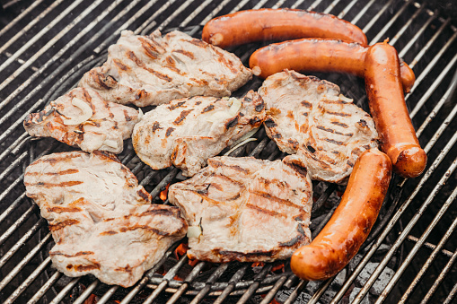 Pieces of pork tenderloin, steaks and sausages on the grill grates. Picnic in nature. Grill food.