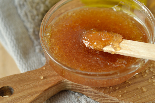 Close-up of homemade lip scrub made out of brown sugar, honey and olive oil in glass bowl on wooden chopping board - Natural beauty product
