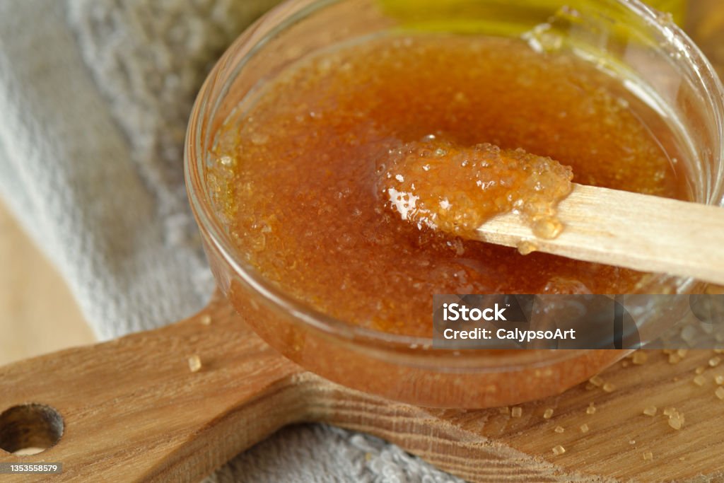Close-up of homemade lip scrub made out of brown sugar, honey and olive oil in glass bowl on wooden chopping board - Natural beauty product Exfoliation Stock Photo