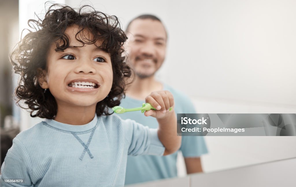 Shot of an adorable little boy brushing his teeth in a bathroom with his father at home I brush up and down and round and round Dental Health Stock Photo