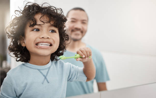 Shot of an adorable little boy brushing his teeth in a bathroom with his father at home I brush up and down and round and round toothbrush stock pictures, royalty-free photos & images