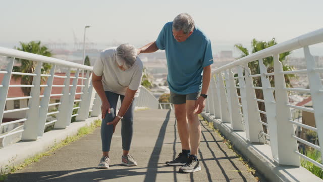 4k video footage of an attractive senior woman suffering injury while out on a run with her husband in the city
