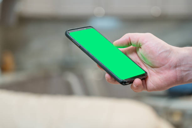 istock Businessman using phone for browsing social networks sitting on home office. Smartphone with green chroma key screen 1353564726
