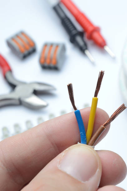 istock stripped, electrical three-core wire in hand against the background of terminal blocks and tools. close-up. 1353565557