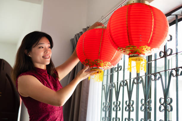 donna asiatica appende grandi lanterne rosse a casa e si prepara a festeggiare il capodanno cinese. - cheongsam chinese culture indoors looking at camera foto e immagini stock