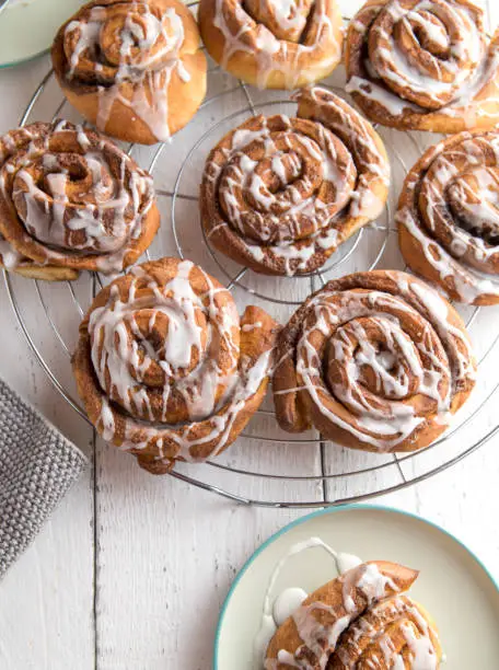 Fresh baked cinnamon rolls on a cooling rack on white wooden table. Closeup and overhead view