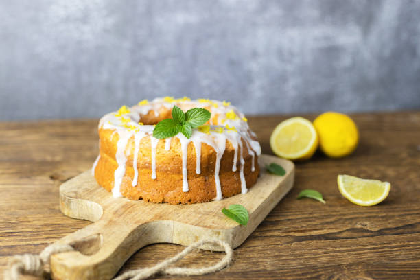 classic lemon loaf cake on a wooden board, garnished with frosting and lemon shavings. fast and tasty dessert - paastaart stockfoto's en -beelden