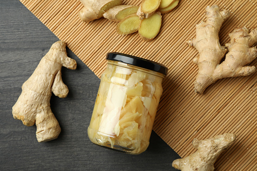 Jar of pickled ginger and ginger on dark wooden background