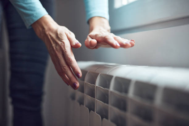 mulher aquecendo as mãos no radiador durante dias frios de inverno. - heating element - fotografias e filmes do acervo