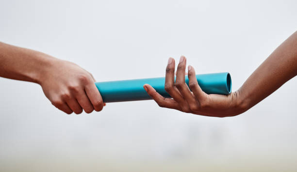 Shot of two athletes passing a baton during a relay race Passing the baton to future generations relay stock pictures, royalty-free photos & images