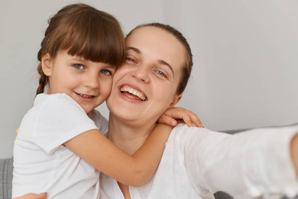 istock Extremely happy smiling female taking selfie with charming dark haired daughter, looking smiling at cell phone camera and hugging point of view photo, family posing at home. 1353570824