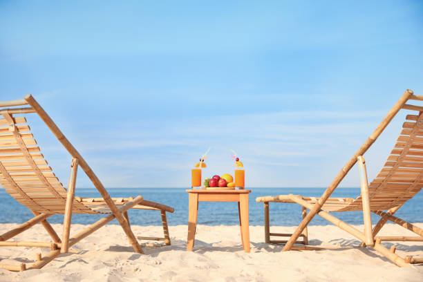 chaises longues en bois près de la table avec des fruits et des boissons sur la plage - beach table peach fruit photos et images de collection