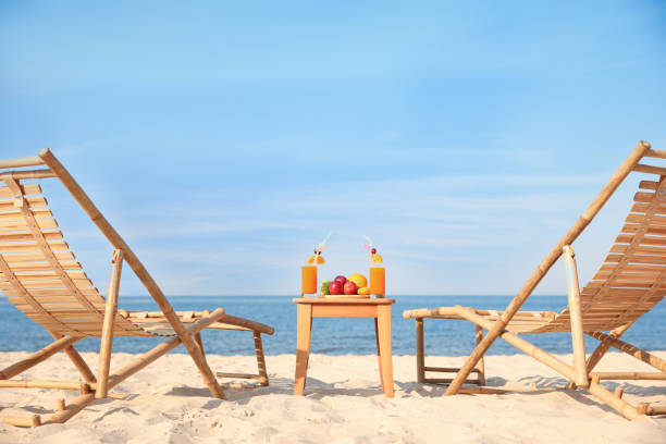 sedie a sdraio in legno vicino al tavolo con frutta e bevande sulla spiaggia - beach table peach fruit foto e immagini stock