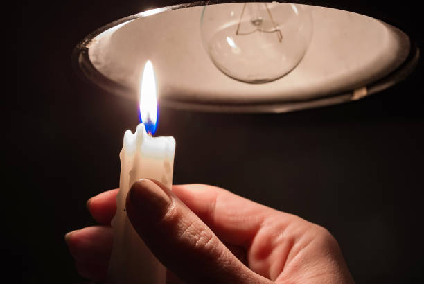 istock A woman's hand with burning candle in complete darkness looking on a switched off light bulb at home. 1353577782