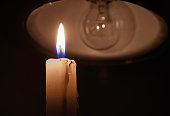 Burning candle near a switched off light bulb in complete darkness.
