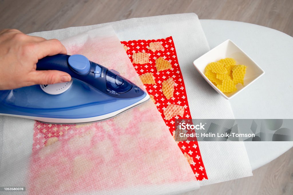 Close up view of person woman make beeswax wraps for wrapping food in home indoors, alternative for plastic. Use iron machine to melt beeswax into cotton cloth. Beeswax Wrap Stock Photo