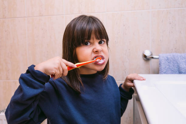 menina de moletom azul escuro, escovando os dentes, no banheiro. escovação de dentes, higiene e conceito de infância. - toothbrush dental hygiene glass dental equipment - fotografias e filmes do acervo