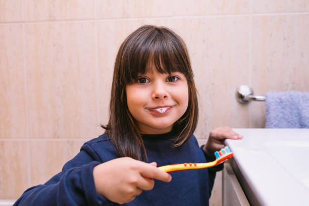 istock Little girl in dark blue sweatshirt, brushing her teeth with toothpaste on her lips, in the bathroom. Tooth brushing, hygiene and childhood concept. 1353580236