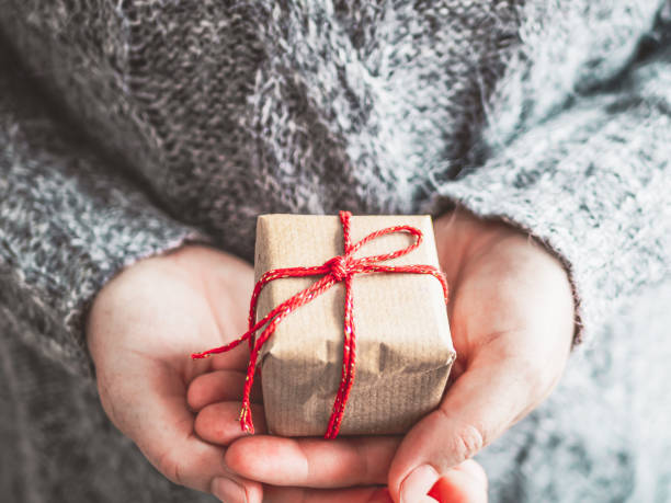 istock Woman is holding a small gift package with a red bow in her hands 1353585963