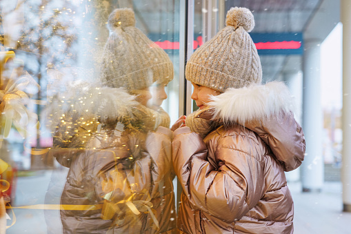little child looks at a Christmas decorated shop window