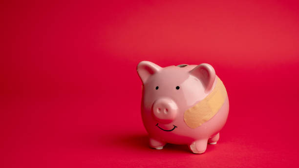 istock Broken piggy bank with beige adhesive on red background. 1353594609