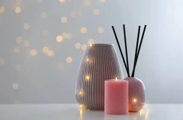 Vase, burning candle and reed diffuser on table against blurred background with bokeh effect. Space for text