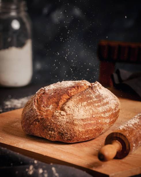 Baked Sourdough Bread on a Chopping Board with Dark Background Sourdough bread on a chopping board with dusted flour and rolling pin. View with fresh milk on a dark background yeast starter stock pictures, royalty-free photos & images