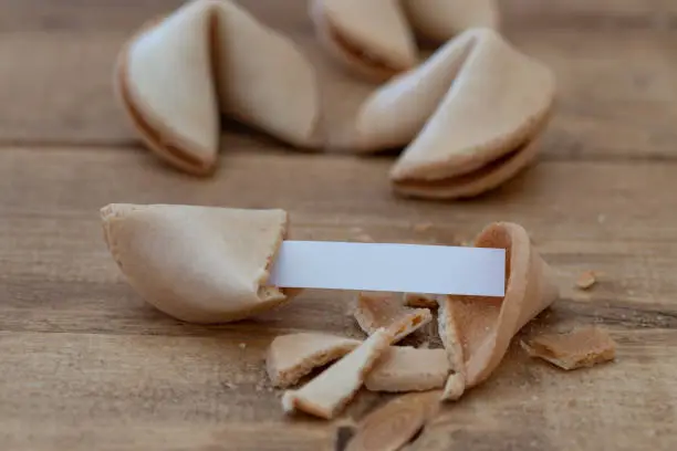 close-up of a broken fortune cookie with a blank paper strip, focus on foreground, closed fortune cookies on the background