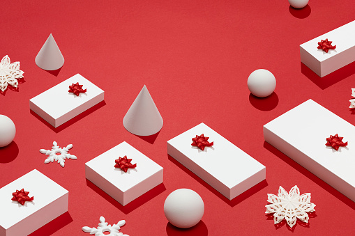 White gift boxes on Christmas concept red background with geometric objects, cone, sphere and snowflake flat lay.