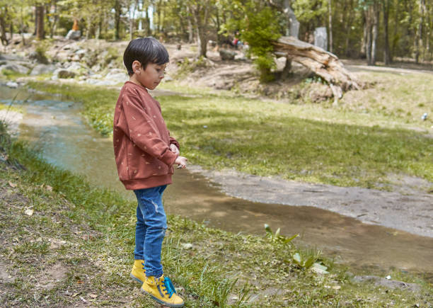 istock Brunette latin boy alone standing in profile looking at a stream reflective, thoughtful. urban clothing. Horizontal. Forest in Argentina 1353598859