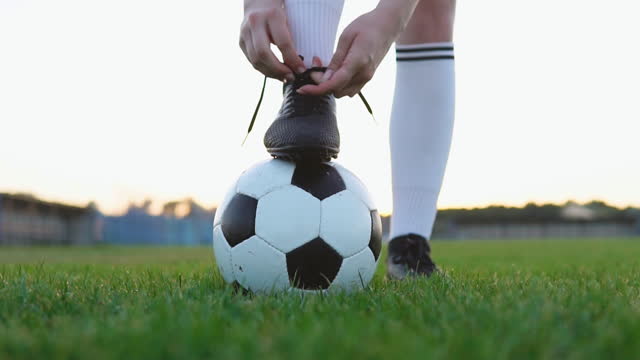 Close up of a female soccer player tying shoelace on football field, slow motion