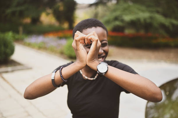 Close up portrait of attractive happy smiling young natural beauty short haired African woman wearing black t-shirt laughing stretching out hands closing from camera in nature summer park. stock photo