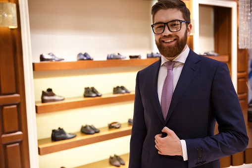 Happy businessman in suit and glasses stading near shelf with shoes