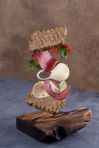 Delicious Sandwich with floating ingredients on the wooden background.