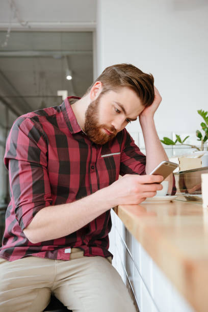 istock Upset young man with smartphone and coffee 1353604796