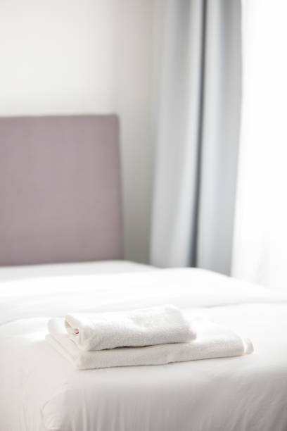 Stock photo showing close-up view of pile of folded, white towels sitting on hotel room duvet bedding.