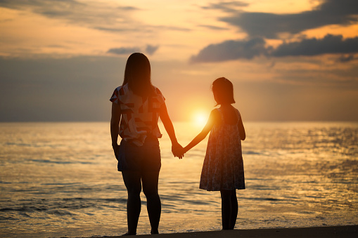 Silhouettes of mother and daughter playing on the beach sunset evening sky background
