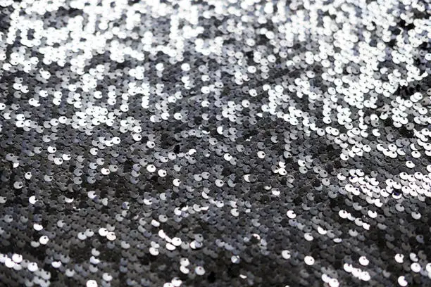 Sequin fabric texture. Shiny silver sparkling background. Clothing piece of glitter metallic for a glamorous party, celebration. Close-up