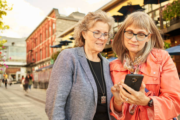 istock Smiling mature female friends using a smart phone while walking in the city 1353612879