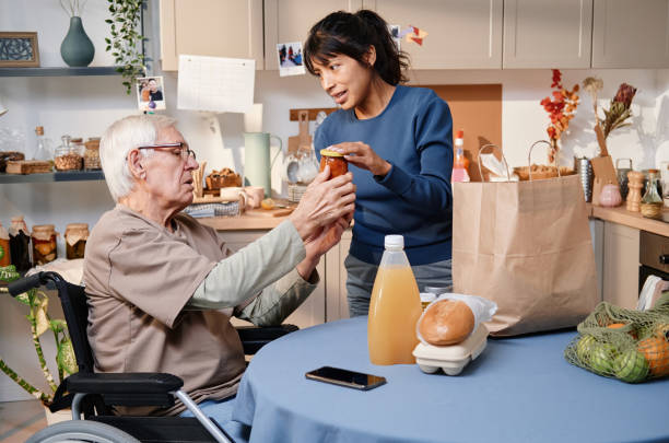 Woman buying food for senior man Volunteer delivering food for senior man who using wheelchair, they sitting in the kitchen and discussing food home caregiver stock pictures, royalty-free photos & images
