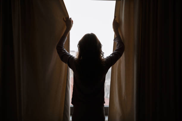 istock Silhouette of woman closes curtains 1353614323
