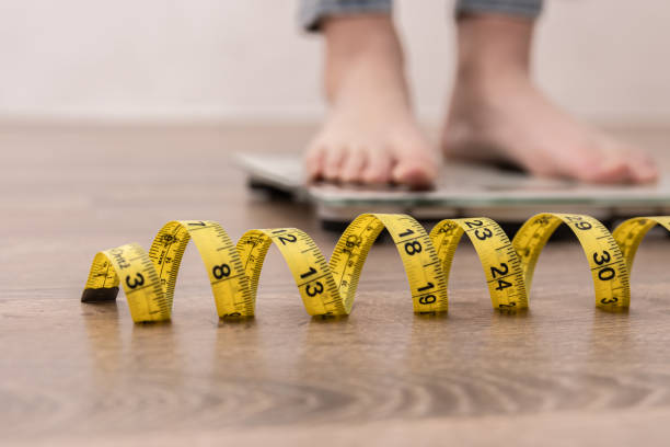 Female leg stepping on weigh scales with measuring tape. Women's legs on the scales, close-up of a measuring tape, the concept of losing weight, healthy lifestyle. photos of anorexia pictures stock pictures, royalty-free photos & images