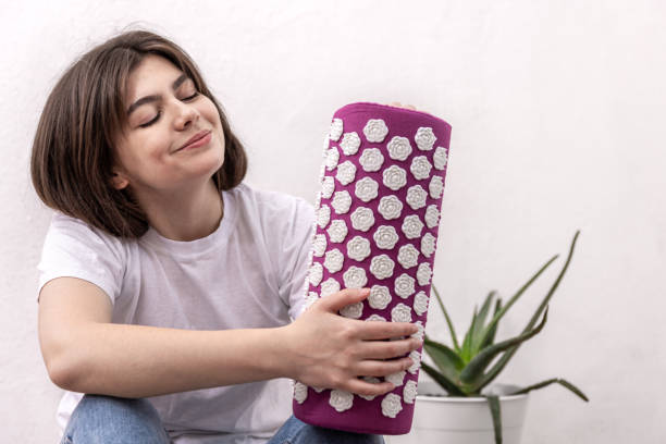 A young woman holds a neck massage pillow. Purple massage acupuncture pillow and white massage tips in female hands. acupuncture mat stock pictures, royalty-free photos & images