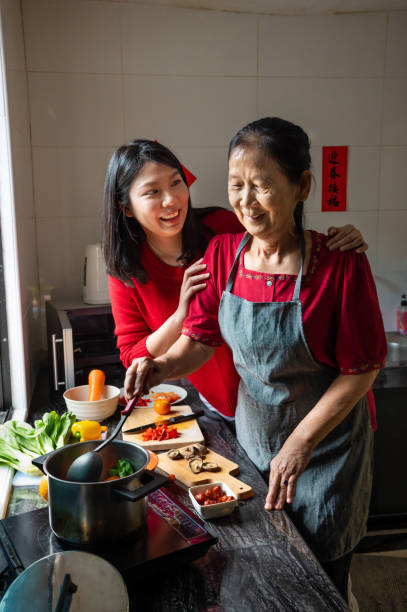 台所で中国の大晦日に食べ物を準備するシニアアジアの女性と彼女の娘 - 25 30 years ストックフォトと画像