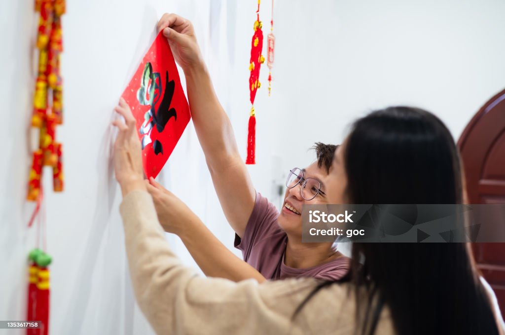 Mid-aged Asian woman helping her brother pasting a Chinese auspicious wording  “Fortune” spring couplet on wall and get prepared for Chinese New Year celebration. Chinese New Year Celebration and Chinese Traditional Festival, Family Reunion, Bonding and Togetherness Concepts. Chinese New Year Stock Photo