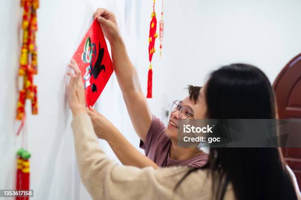 Midaged Asian Woman Helping Her Brother Pasting A Chinese Auspicious Wording Fortune Spring Couplet On Wall And Get Prepared For Chinese New Year Celebration Stock Photo - Download Image Now