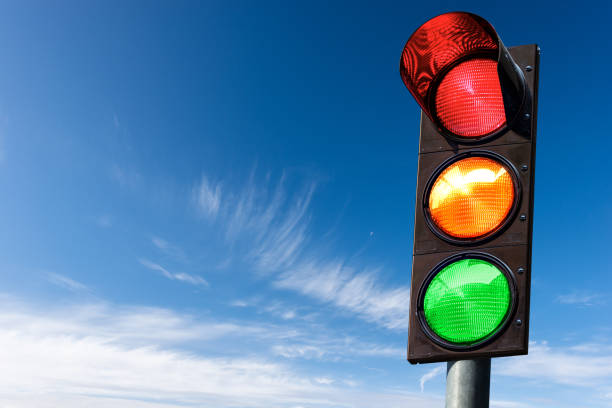 Traffic Light against a Blue Sky with Clouds and Copy Space Closeup of a traffic light on a blue sky with clouds and copy space, with all three lights on, green, orange and red. Italy, Europe. blue yellow lights stock pictures, royalty-free photos & images