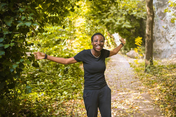 Attractive happy smiling young natural beauty short haired African woman wearing total black walking and dancing in nature green summer park. Diversity concept. stock photo
