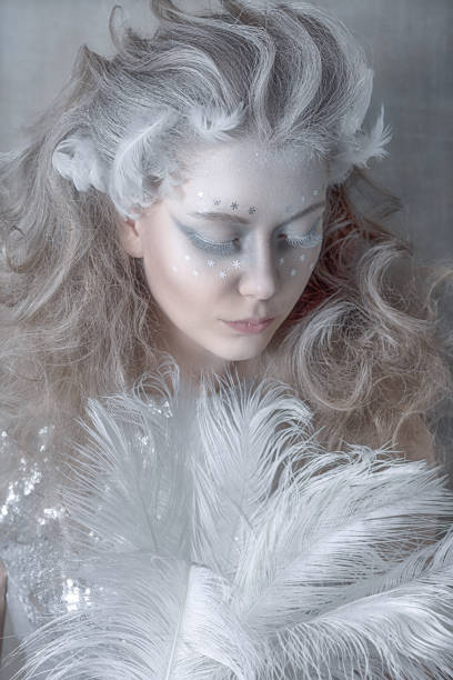 красивая девушка в образе белого ле�бедя в серебряном платье с белыми перьями в руках снежной королевы. портрет роскошной блондинки. креати� - snow maiden стоковые фото и изображения